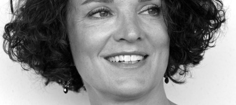 Porträtfoto von Lucía Baumgartner. Ihr lachendes Gesicht ist von dunkeln Locken gerahmt.