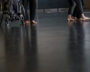 Füsse und Knie von vier Personen nebeneinander, drei stehend, eine sitzend im Rollstuhl.