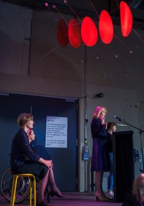 Er&ouml;ffnungsansprache der Stadtpr&auml;sidentin Marieke Kruit am Rednerpult.  Sie steht an einem Rednerpult.  An der Decke h&auml;ngt eine leuchtend rote Installation.
